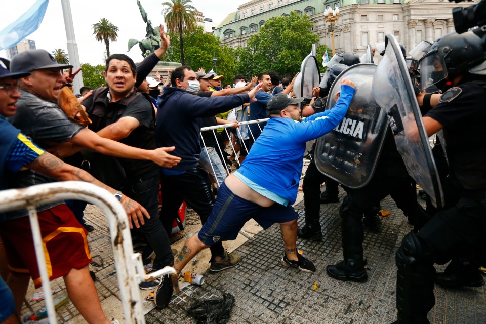 One fan pounds on the shield of a riot cop as they try to get a glimpse of their hero’s casket at the presidential palace