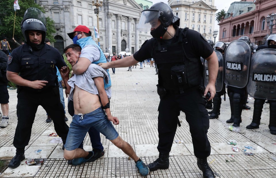 Police detain a man during clashes while fans wait to enter the Government House