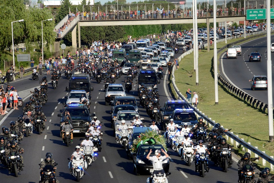 People stand on the bridge and the highway as a large number of security vehicles escort the football player’s hearse on the 25 de Mayo Highway