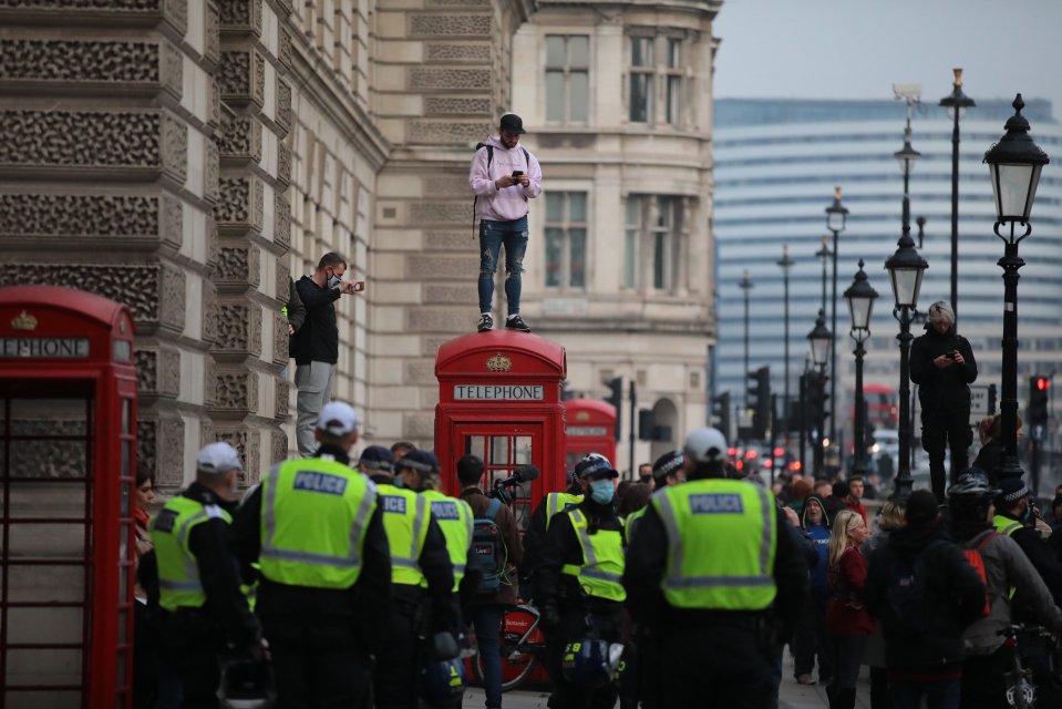 A man stands on top of the telephone booth during anti-lockdown protests in central London