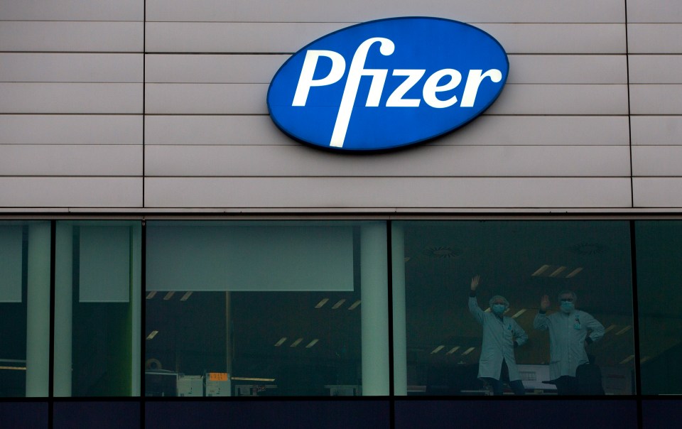 Staff at Pfizer are seen in the windows of the Belgian plant as the lorries leave