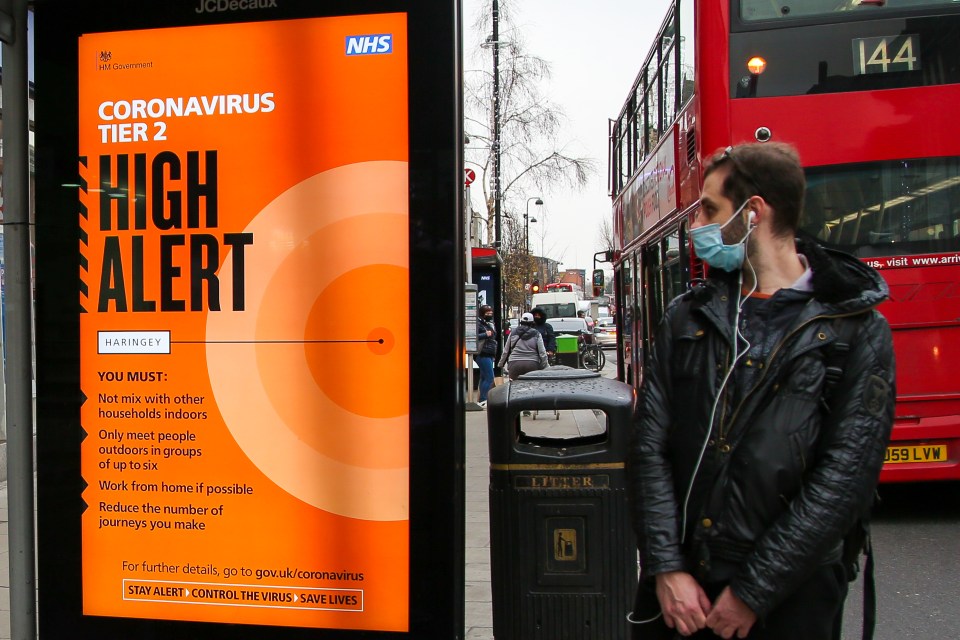 A man wearing face covering looks at 'Tier 2 High Alert' poster in north London