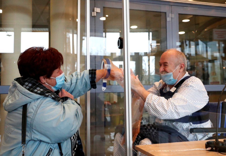 A couple meets behind a plexiglass wall which allows families to give hugs without risk of transmission of Covid-19