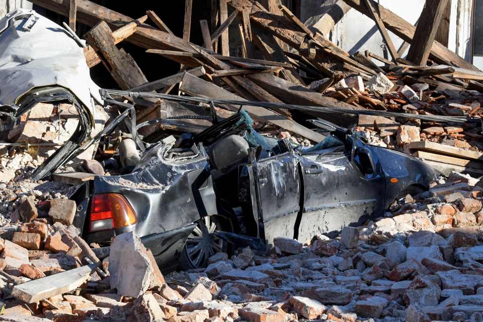 A car is seen crushed by a collapsed building