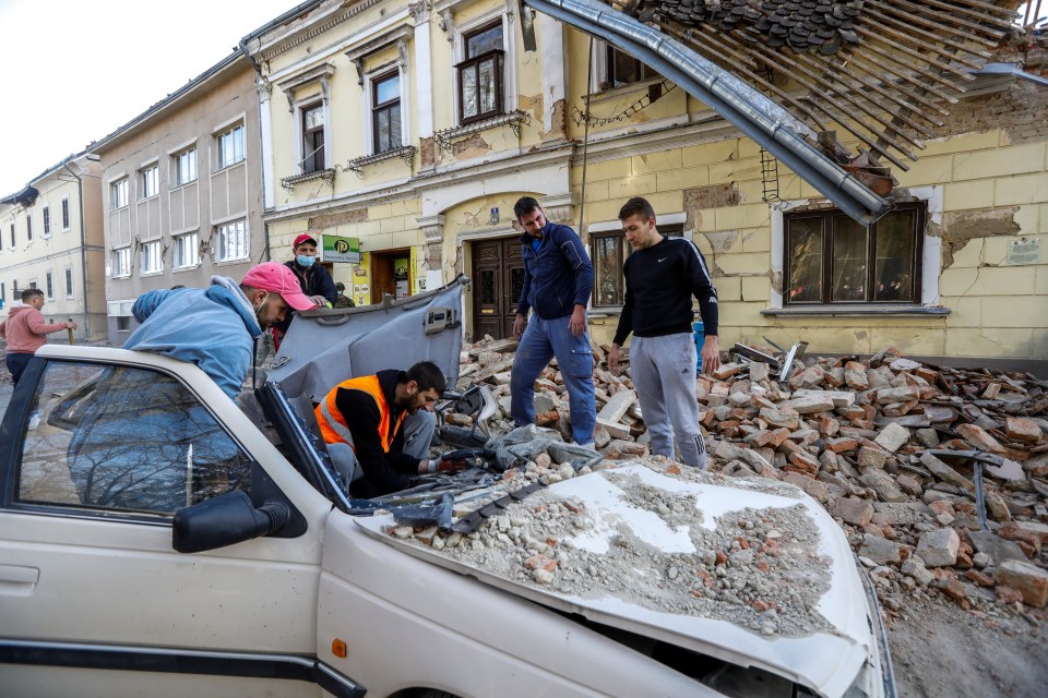 Locals stand around a car damaged by rubble