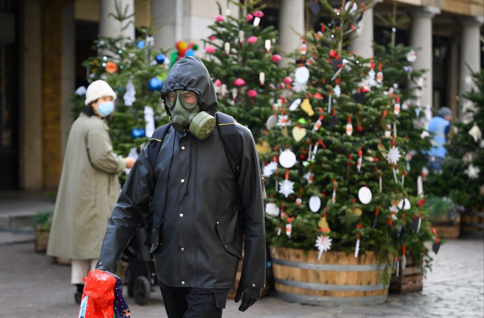 A man wearing full protective clothing and a gasmask walks through the decorated piazza of Covent Garden