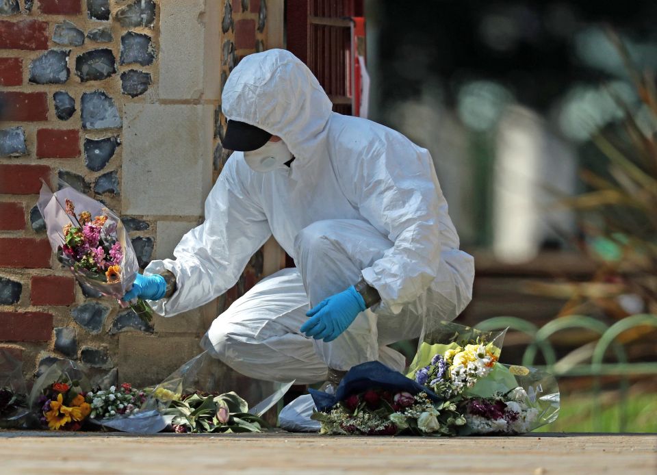 A forensic officer searches floral tributes laid at Forbury Gardens, in Reading town centre