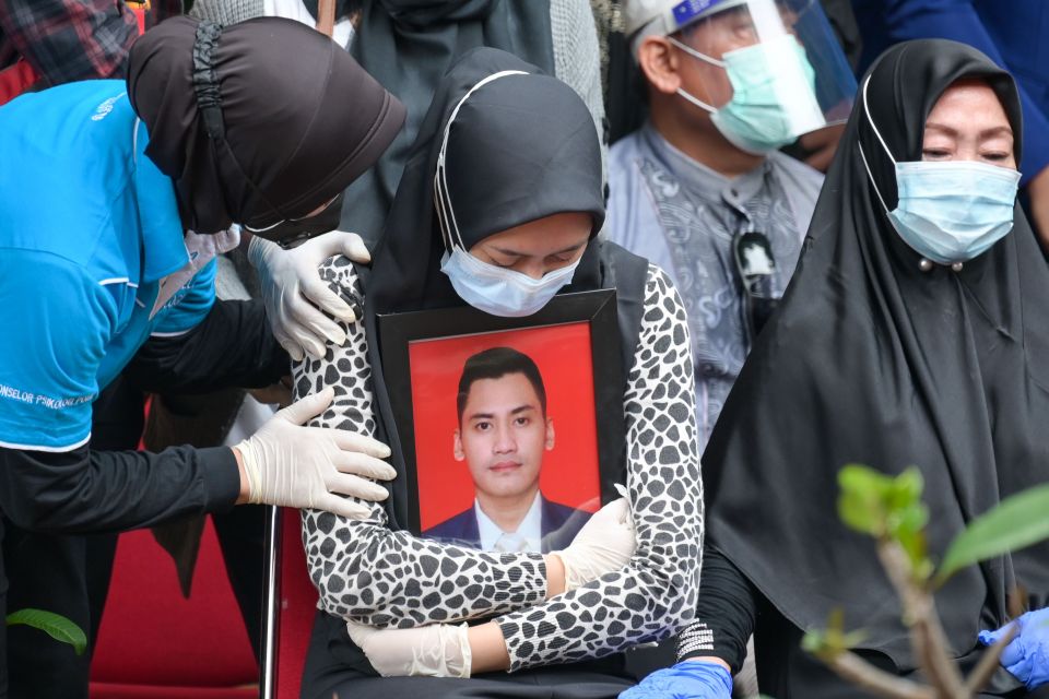 The widow of flight attendant Okky Bisma clutches a picture of him at his funeral today