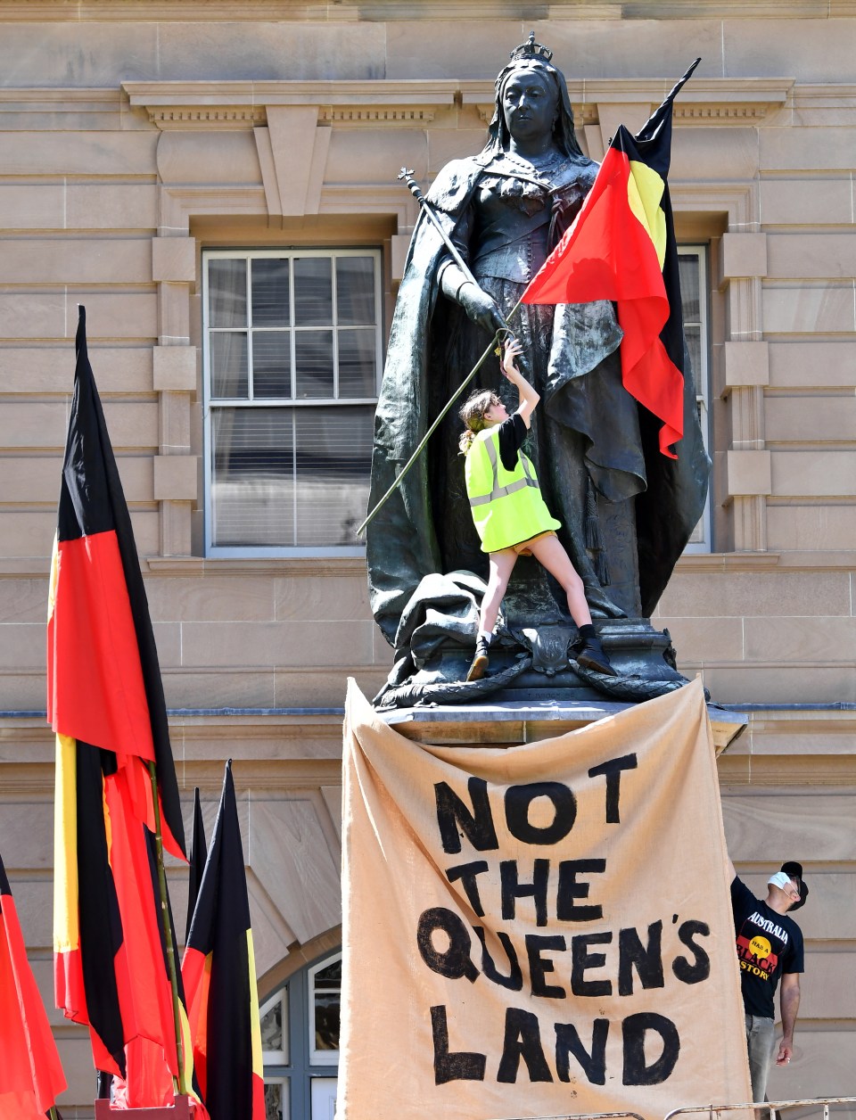 A protester is spotted attaching an Aboriginal flag to a statue of Queen Victoria in Queens Gardens Brisbane