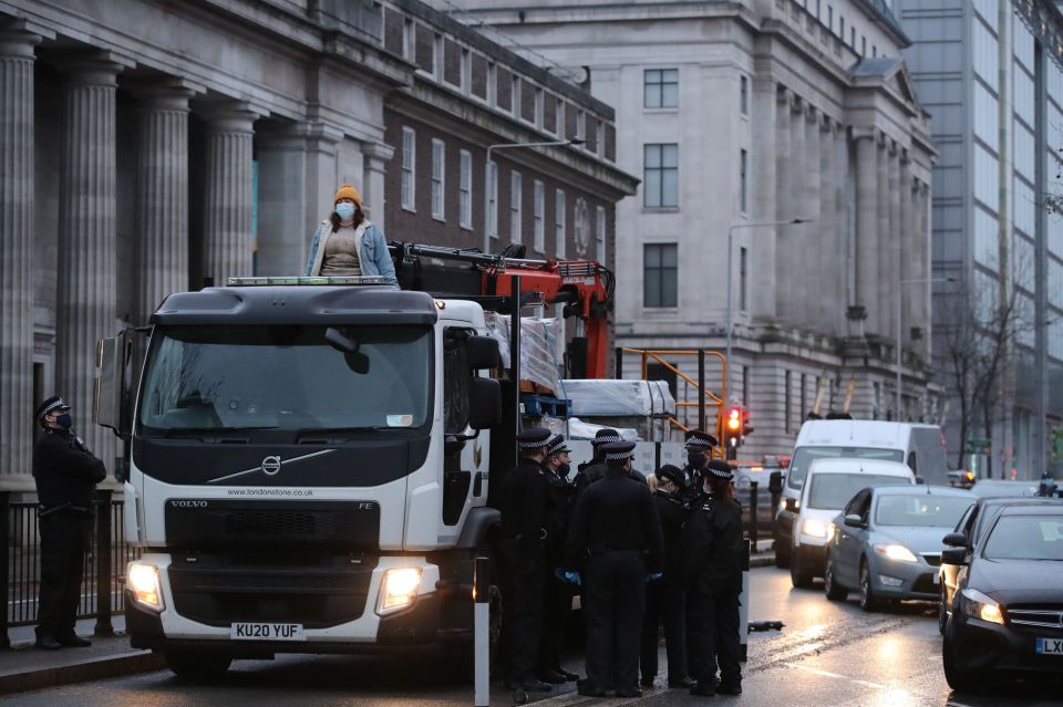 Police officers watch a woman standing on top of a lorry blocking the traffic