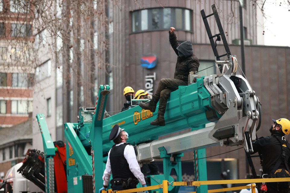 A protester raises their fist while sitting on a crane