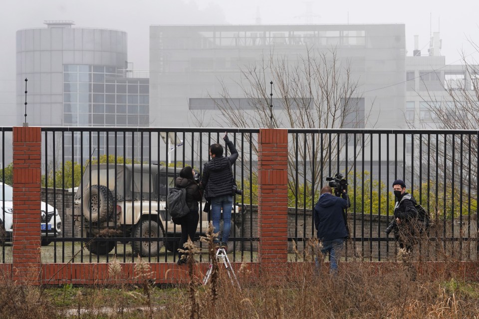 Journalists gather at the fence looking into the Wuhan Institute of Virology