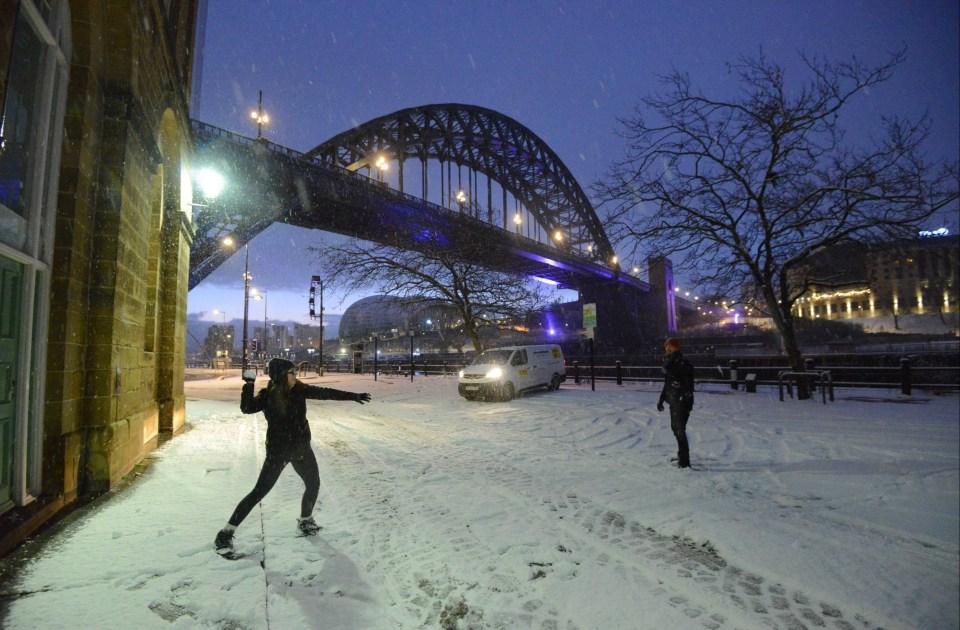 Two joggers take a break from their early morning run to throw snow balls at each other under Newcastle's Tyne bridge this morning