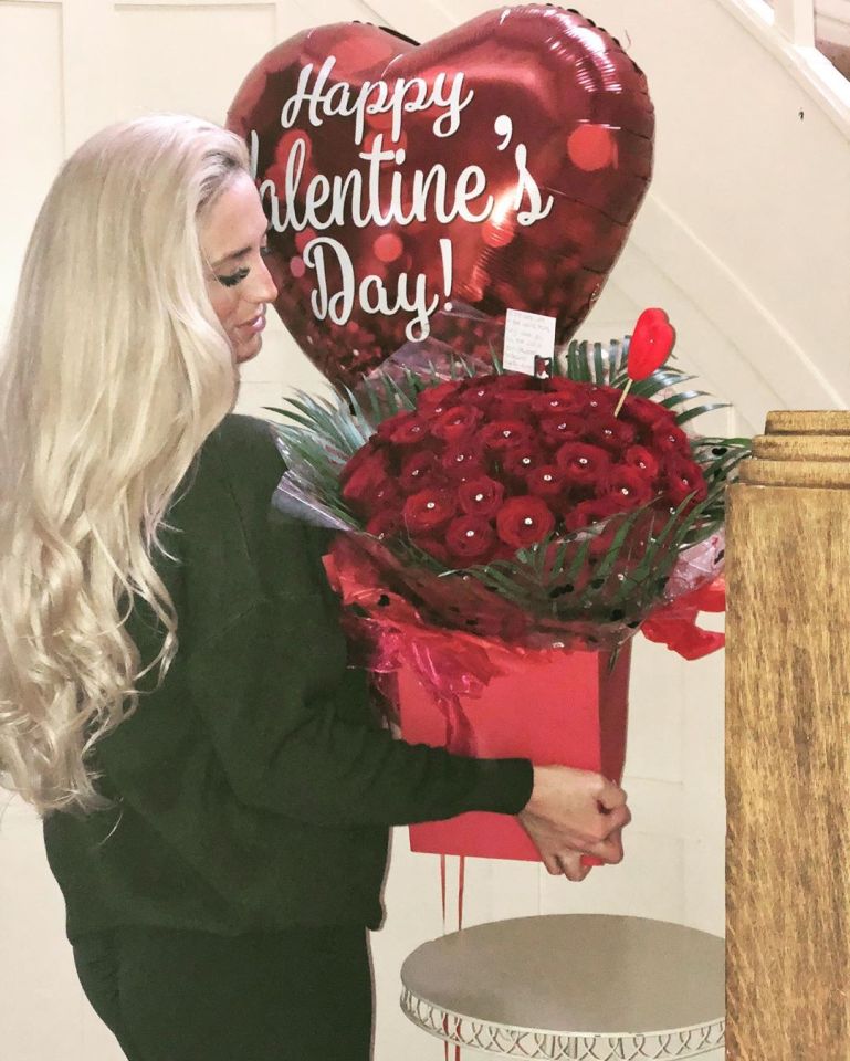 a woman holds a box of red roses and balloons that say happy valentine 's day