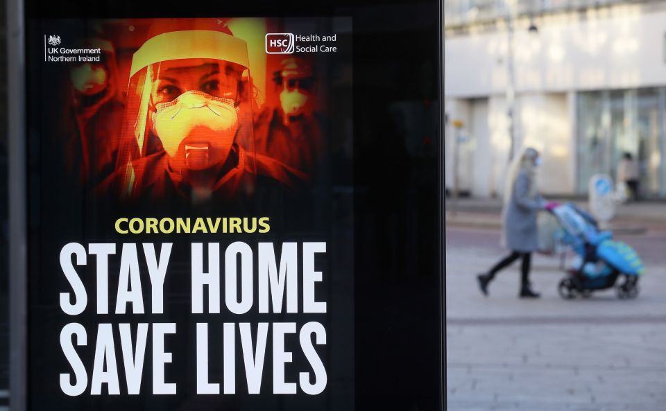 A woman walks past a Government message on a bus stop in Belfast city centre as the six week lockdown in Northern Ireland continues