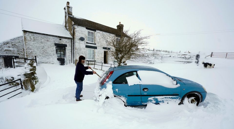 A woman clears the snow from her car in the village of Harwood in Teesdale, Durham