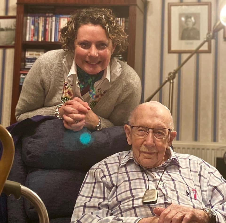 a woman sits next to an elderly man in a chair