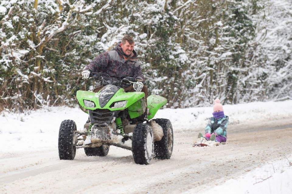 Richard Squirrell uses a quad bike to give his granddaughter Florence a ride in the snow in Wattisham, Suffolk