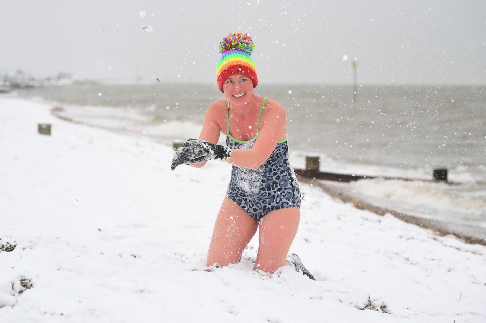 An early morning swimmer plays with the snow at the beach in Thorpe End, Essex