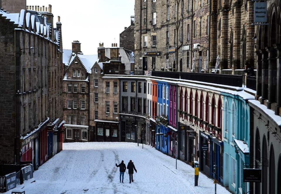 People walk in the snow on the deserted Victoria Street in Edinburgh