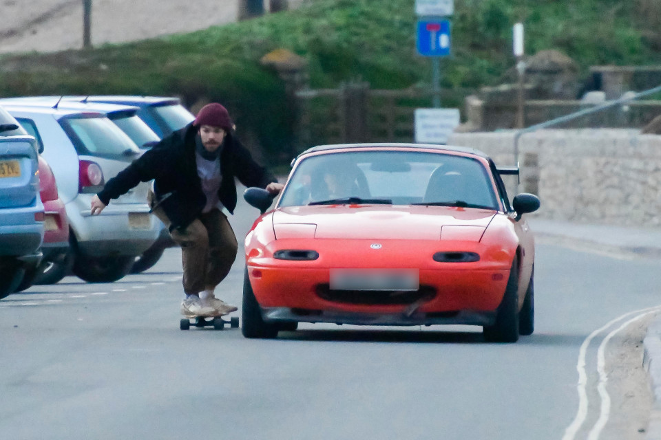 A sketoboarder holds on to the side of car to ride along