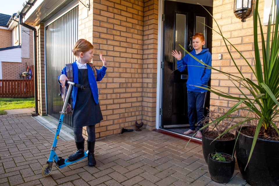 6 year old Ella Williamson waves goodbye to her older brother Jamie (11) as she returns to school (Lainshaw primary in Stewarton, Scotland)