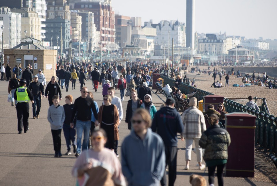 A police officer walks among groups of people as they walk along Hove's seafront