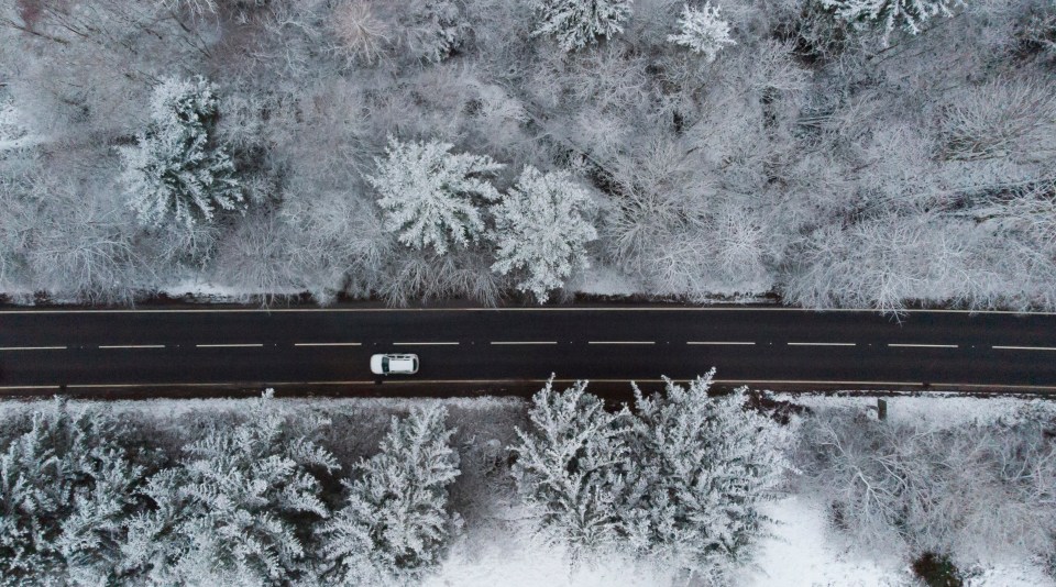 A car drives between snow covered trees on the A470