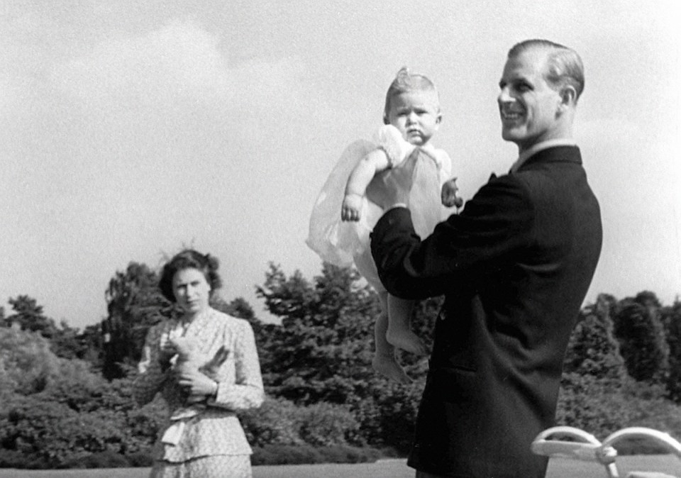 Prince Charles is held by Prince Philip as the Queen looks on