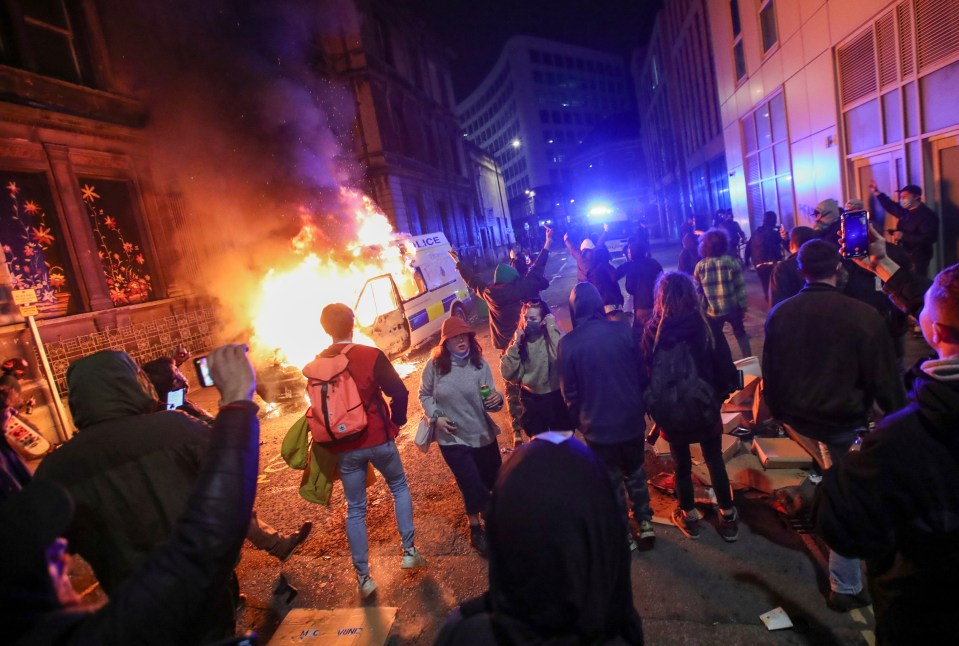 Demonstrators stand near a burning police vehicle during Sunday's protest against a new proposed policing bill