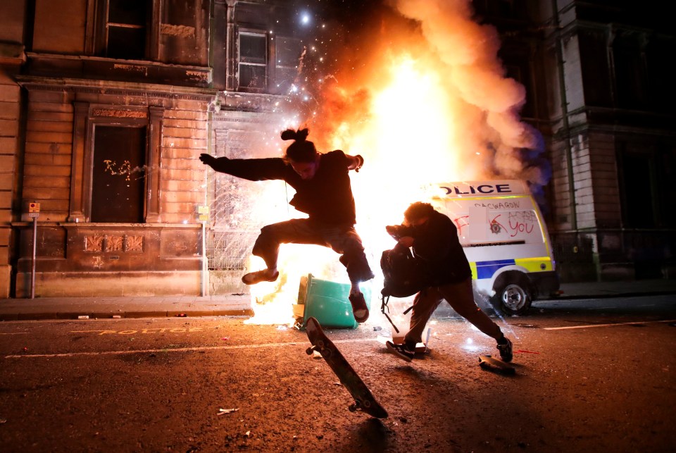 A demonstrator skateboards in front of a burning police vehicle during a protest against a new proposed policing bill