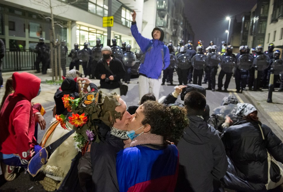 A couple in the crowd share a kiss in front of a line of riot police