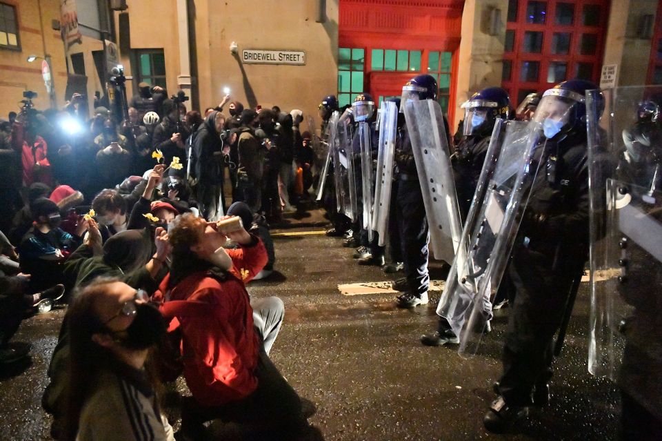 Protesters sit in front of police officers on Bridgewell Street