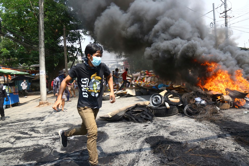 Anti-coup protesters run round a burning barricade as demos continued to rage in Myanmar yesterday