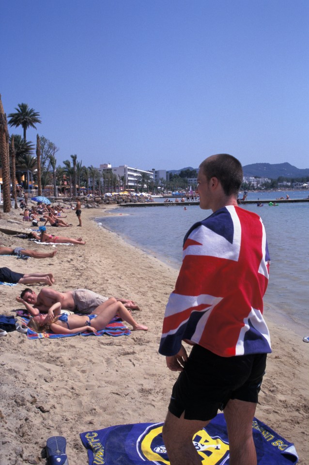 British holidaymaker wrapped in Union Jack flag towel on the beach in San Antonio, Ibiza