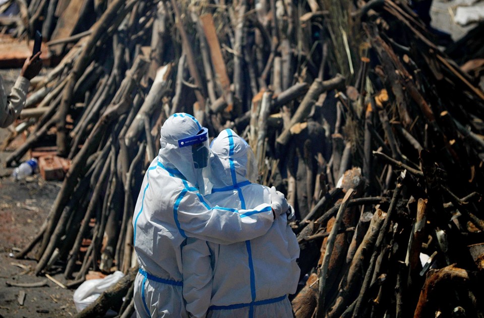 Relatives wearing PPE comfort each other as they watch the burning bodies of loved ones