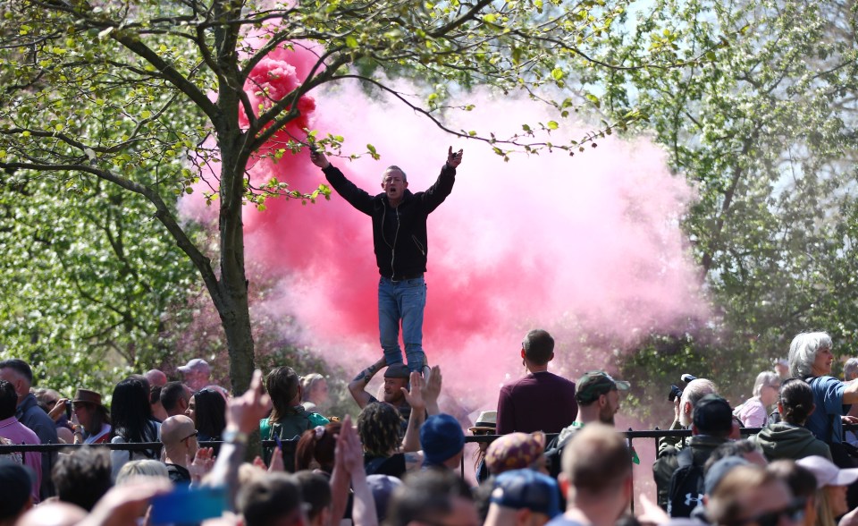 A demonstrator holds a smoke flare as he stands on a man’s shoulders