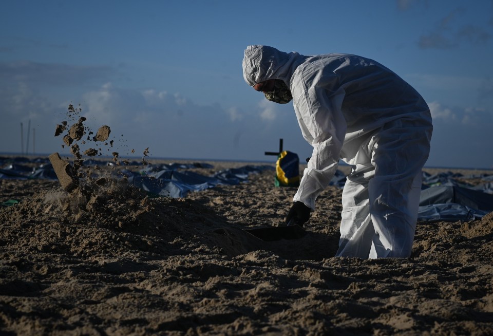 An activist from NGO Rio de Paz digs a grave wearing a biological protection suit in front of death bags during a symbolic act in protest for the memory of the 400,000