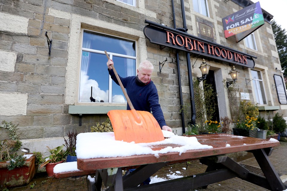 Paul Turner clears away snow from the benches outside the Robin Hood Inn at Pecket Well near Hebden Bridge, West Yorkshire