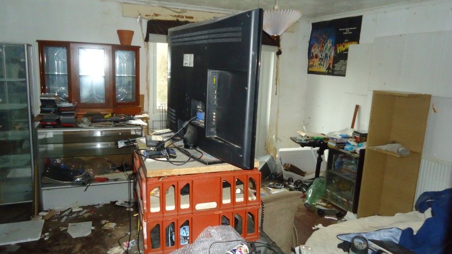 A TV sits on top of a crate with rubbish lining the floor in the home's sitting room