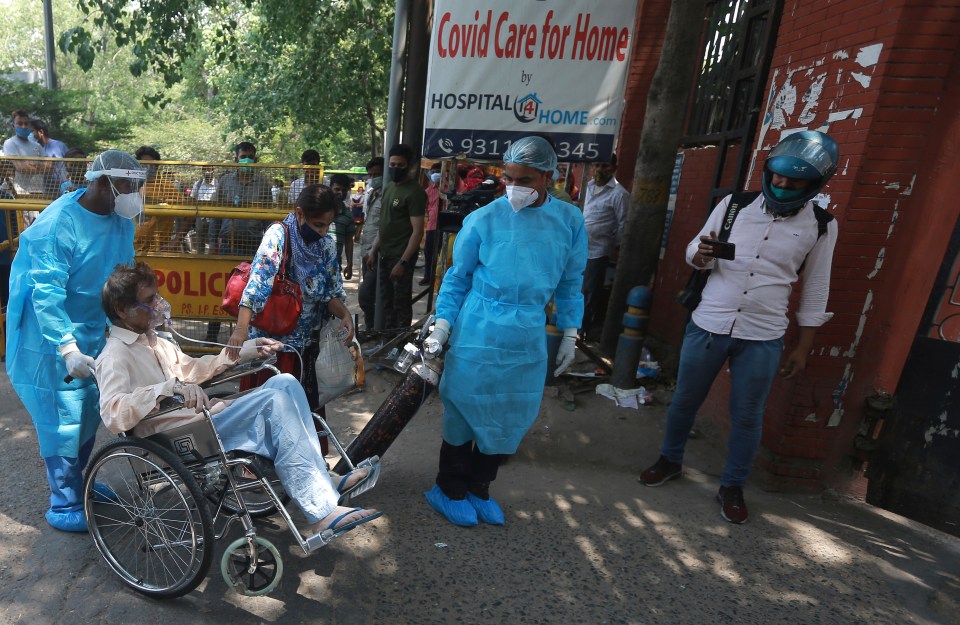 Health workers assist a patient as he is brought to a Covid care center in New Delhi, India