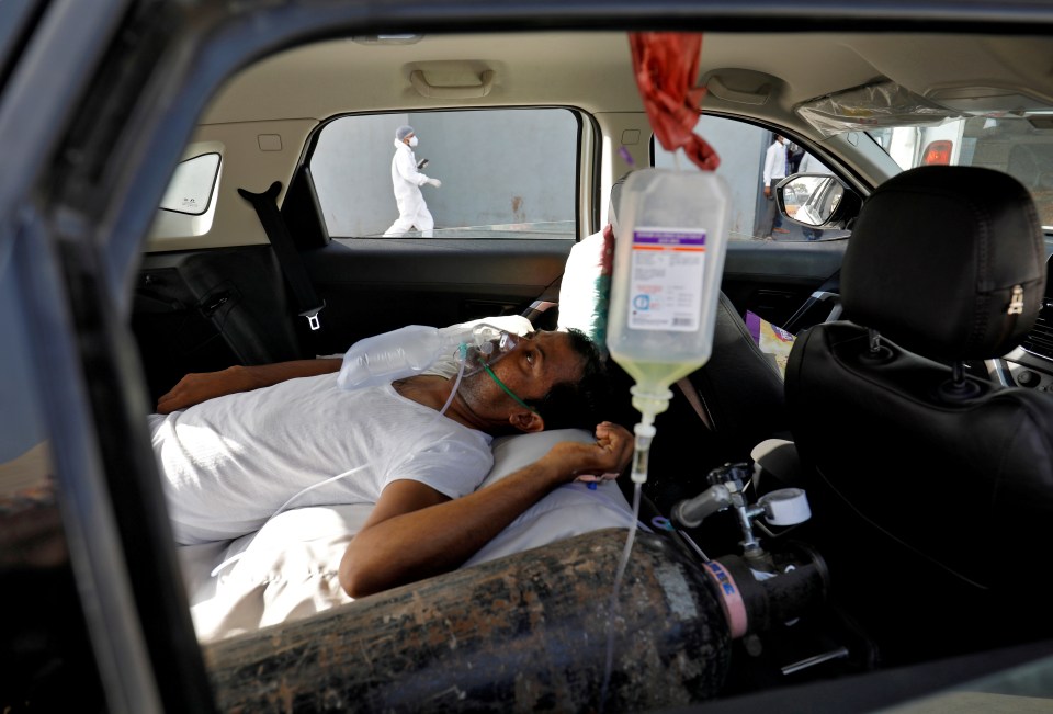 A patient with breathing problems lies inside a car while waiting to enter a Covid hospital for treatment