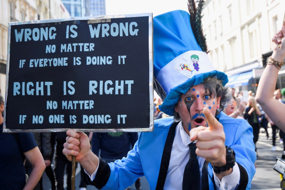 A man wearing a costume holds a sign, as he takes part in an anti-lockdown protest