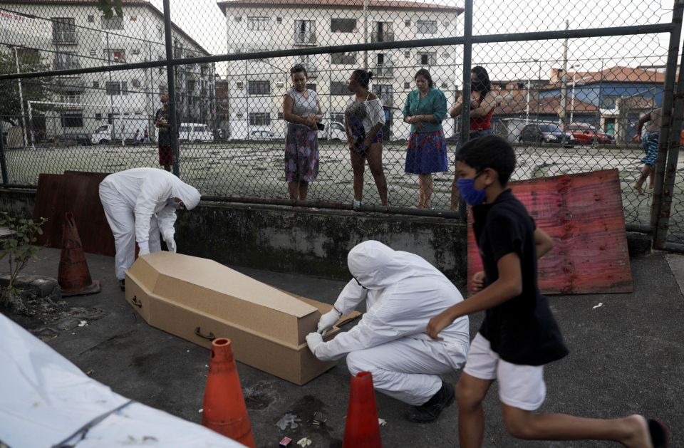 Workers of a funeral parlour, wearing protective clothing, place in a casket the body of Valnir Mendes da Silva, 62