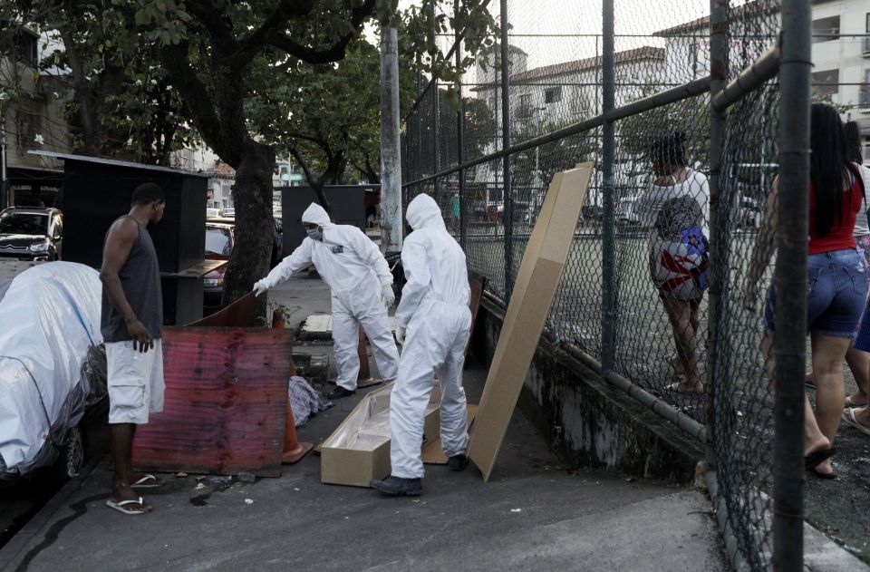 Workers of a funeral parlour, wearing protective clothing, remove the body of Valnir Mendes da Silva, 62, that was laying on a sidewalk of Arara community