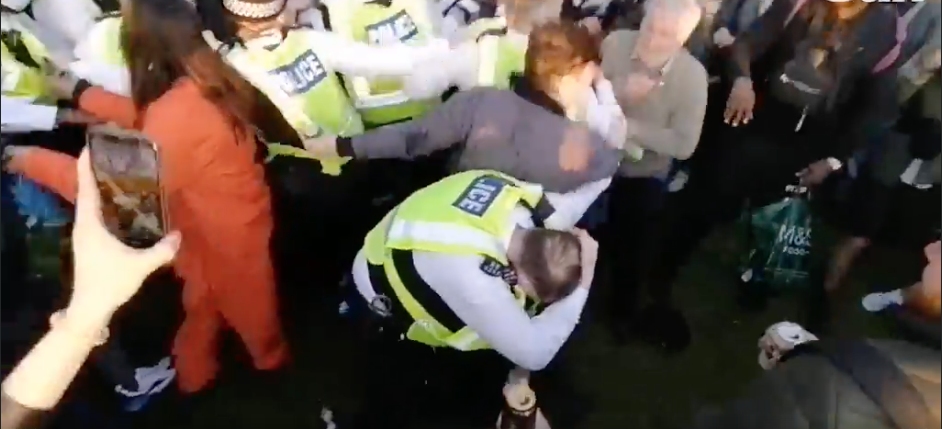 An officer is seen shielding himself from objects as protesters throw bottles and cans