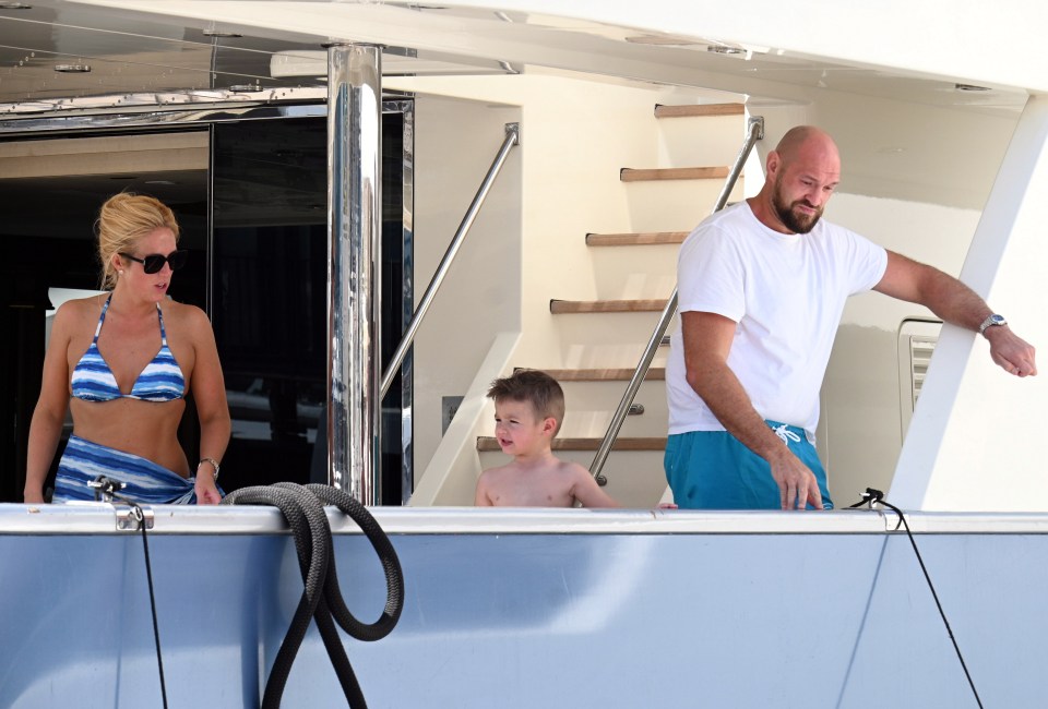 a woman in a bikini stands next to a man and a boy on a boat