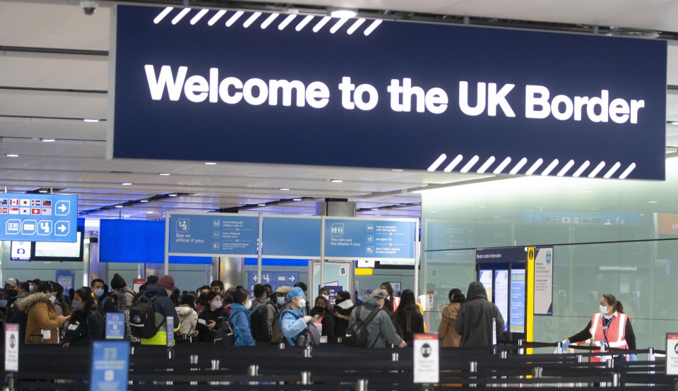 Masked passengers queue at UK border control at Heathrow Airport