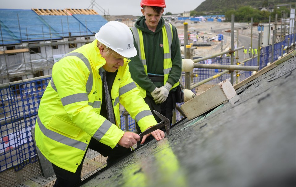 Boris Johnson is shown how to fit roofing tiles during a visit to the West Carclaze Garden Village housing development