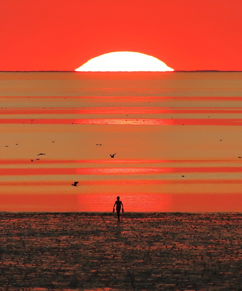 A beautiful end of a hot day as a person goes for a walk on the beach at just before sunset at Heacham, Norfolk